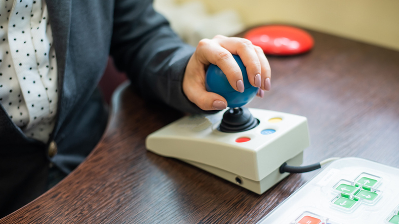 A person's hand using an adaptive joystick switch with large directional buttons